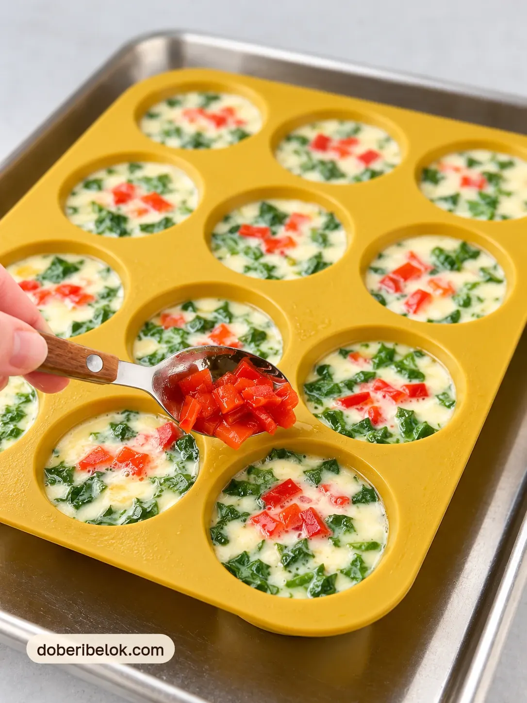 Ложка с деревянной ручкой добавляет кусочки запечённого красного перца в ячейки со шпинатом