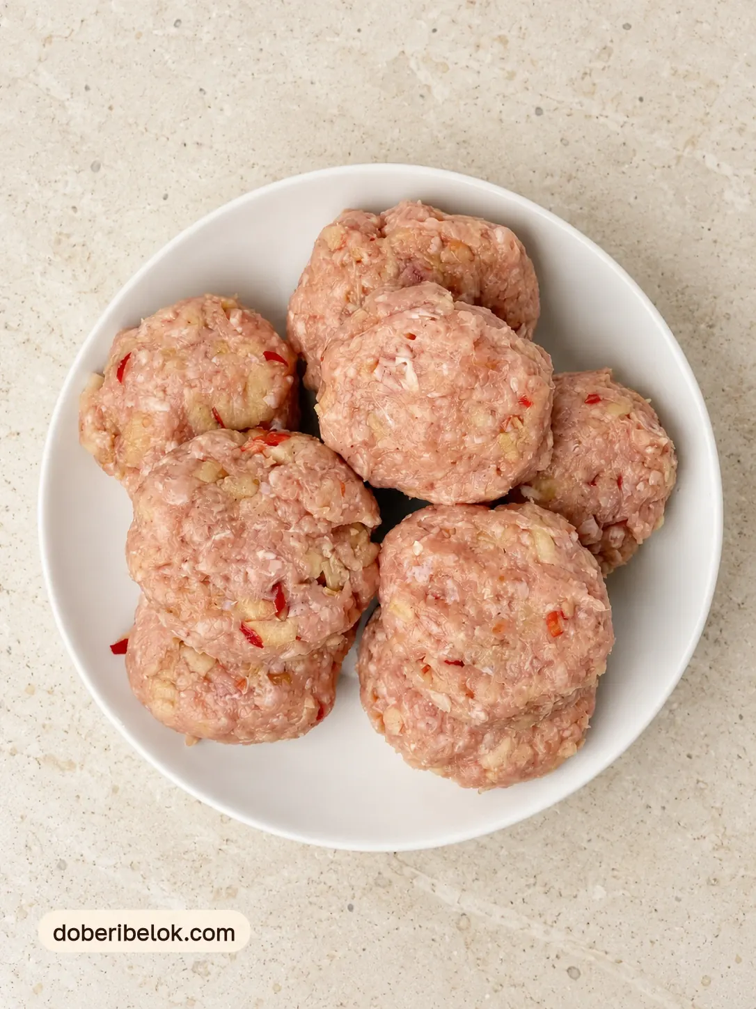 Сырые котлетки из куриного фарша с яблоком на белой тарелке