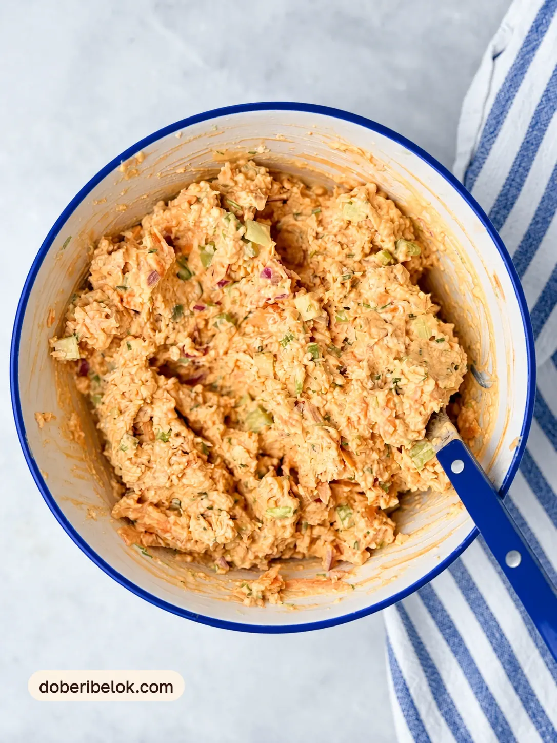 Перемешанный кремовый куриный салат с овощами в миске с синей ложкой