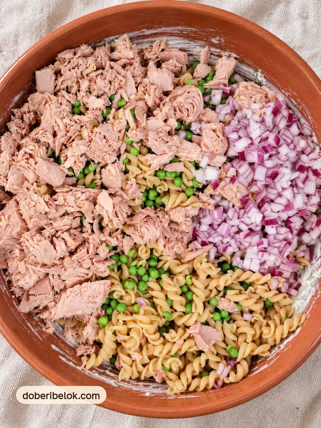Тунец, спиральки с горошком и красный лук в терракотовой миске перед перемешиванием