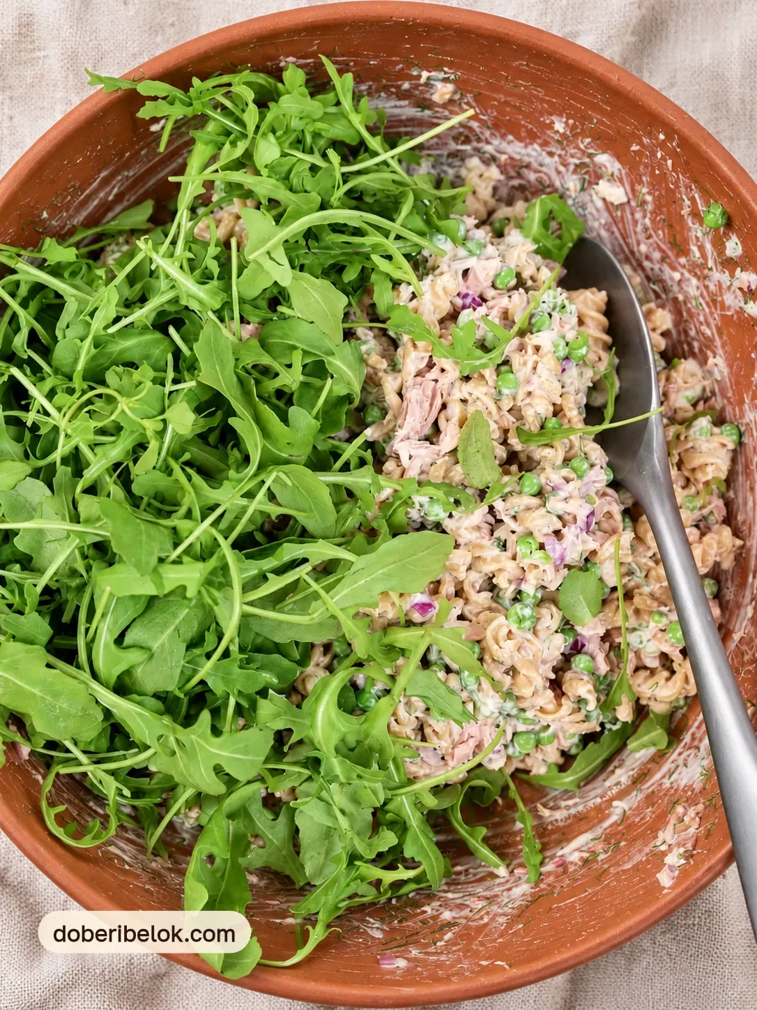 Перемешанный салат с тунцом и макаронами и горка свежей рукколы в терракотовой миске