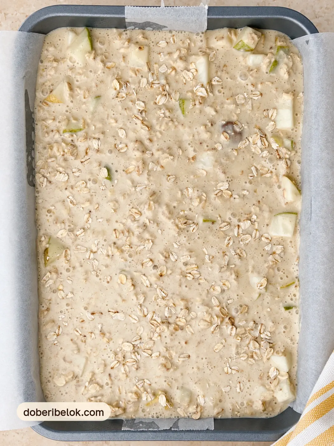 Сырая овсяная масса с кусочками груши в прямоугольной форме с пергаментом, вид сверху